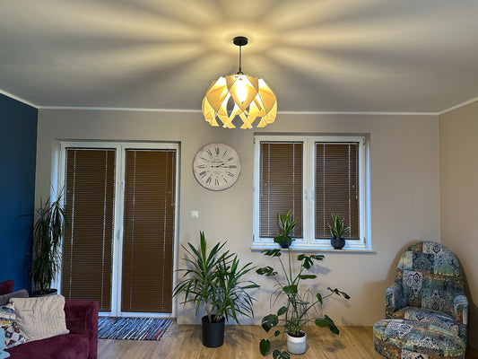 The large wooden pendant lamp hangs from the ceiling, illuminating a living room with warm, diffused light. The lamp's modern, flower-like design casts intricate light patterns on the walls and ceiling.