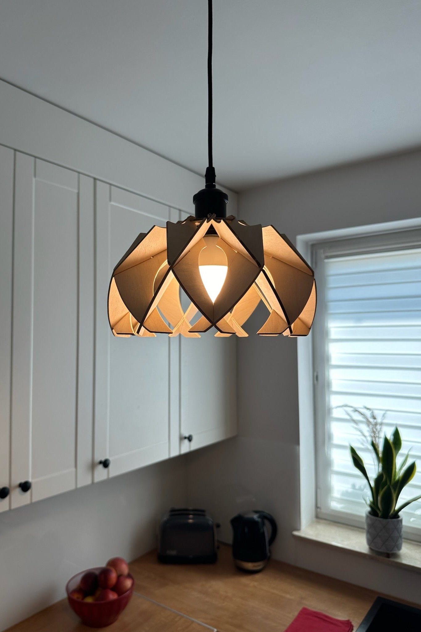 Side view of the natural birch wood small pendant lamp in a kitchen, highlighting the detailed craftsmanship of the wooden petals and the warm, inviting light it emits.