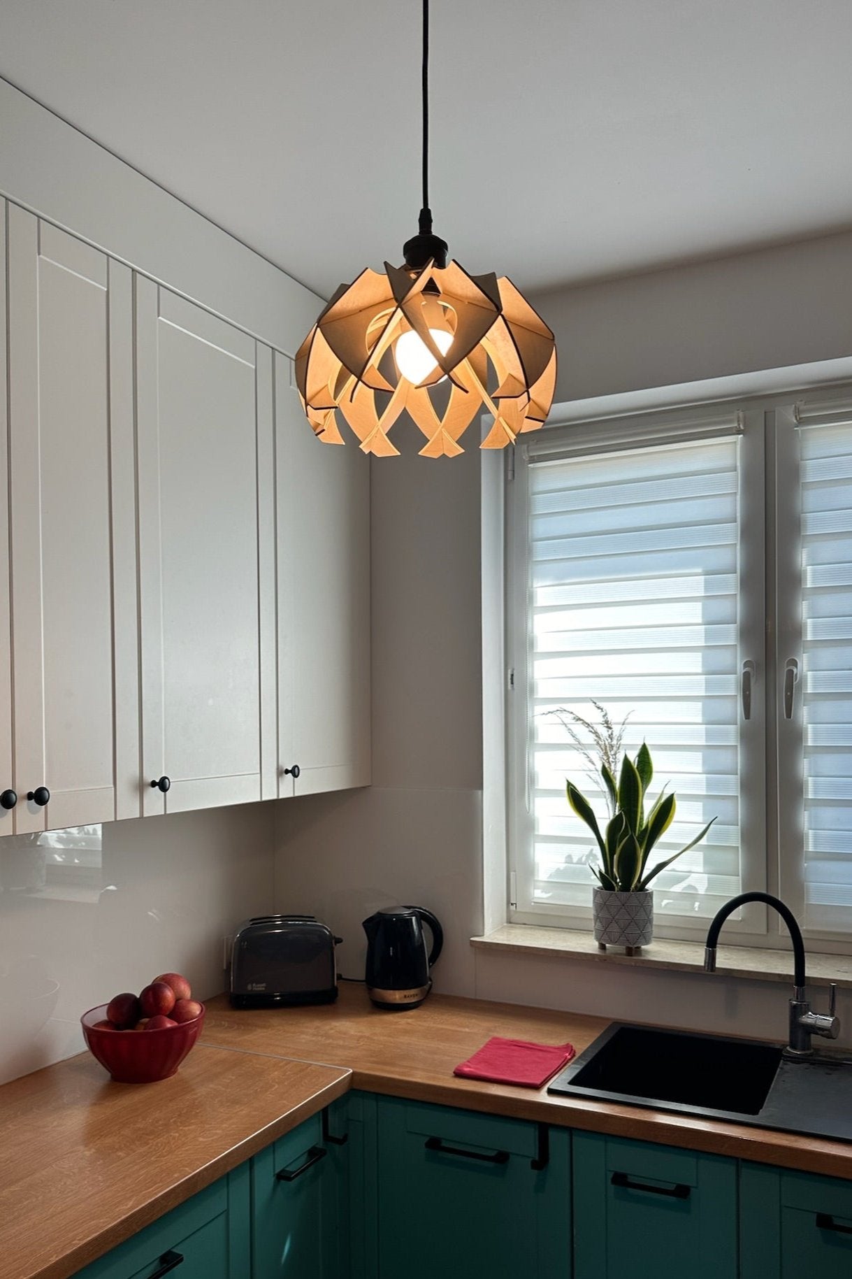 Small natural birch wood pendant lamp in a modern kitchen. The smooth, curved wooden petals form a sleek and contemporary design, casting warm light patterns across the room.