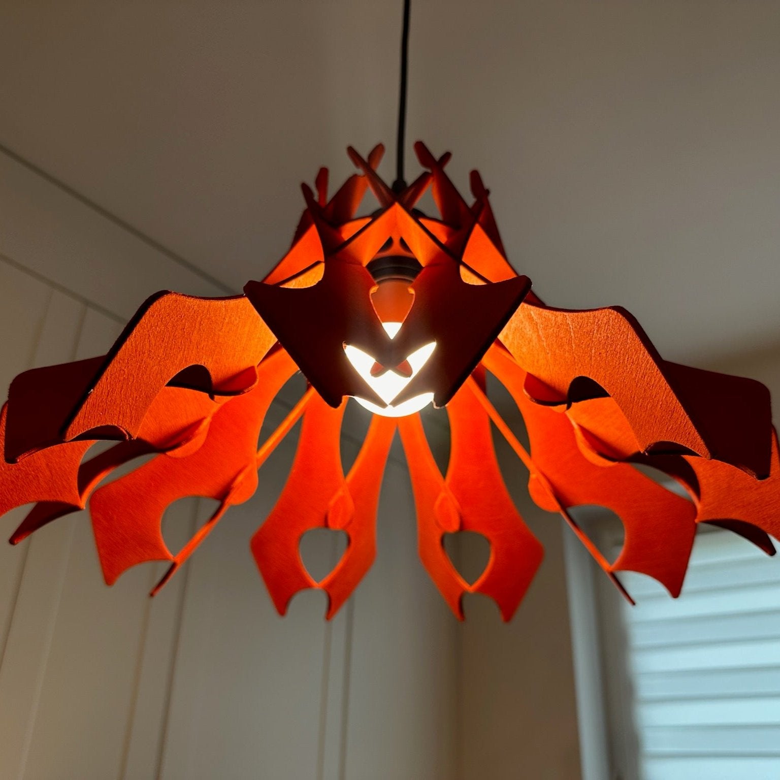 Close-up view of a vibrant scarlet-colored wooden pendant lampshade with unique, curved cutouts and smooth edges. The light inside creates a warm, ambient glow, highlighting the intricate design and craftsmanship.